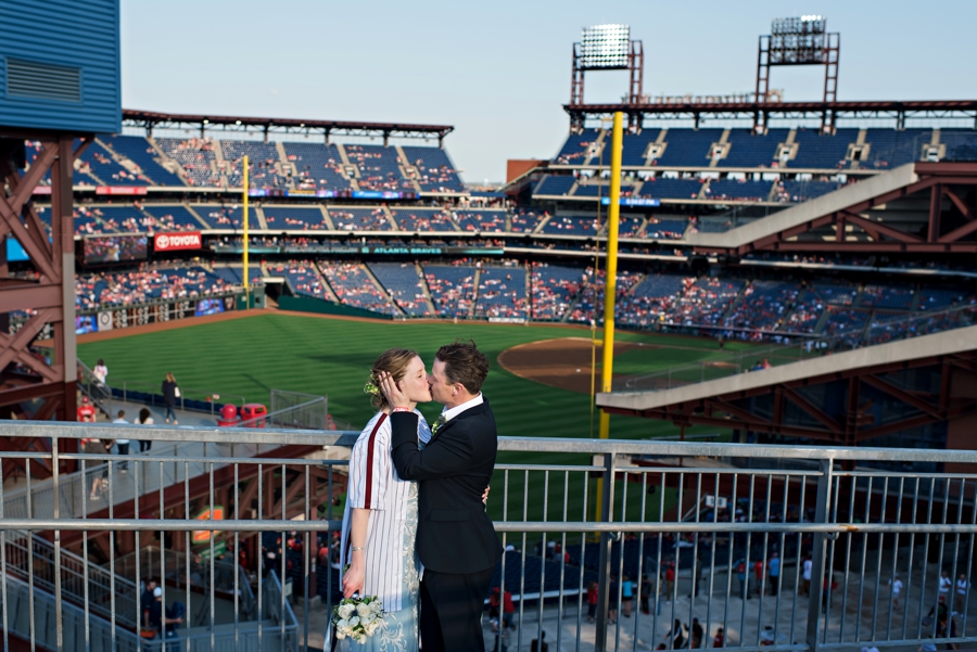 A groom kisses his new bride with the Phillies field behind them.